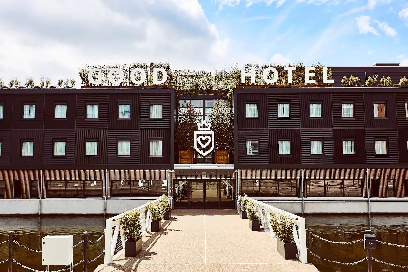 Good Hotel London, moored at Royal Victoria Dock, with GOOD HOTEL in large letters on the roof and a gangway to the entrance
