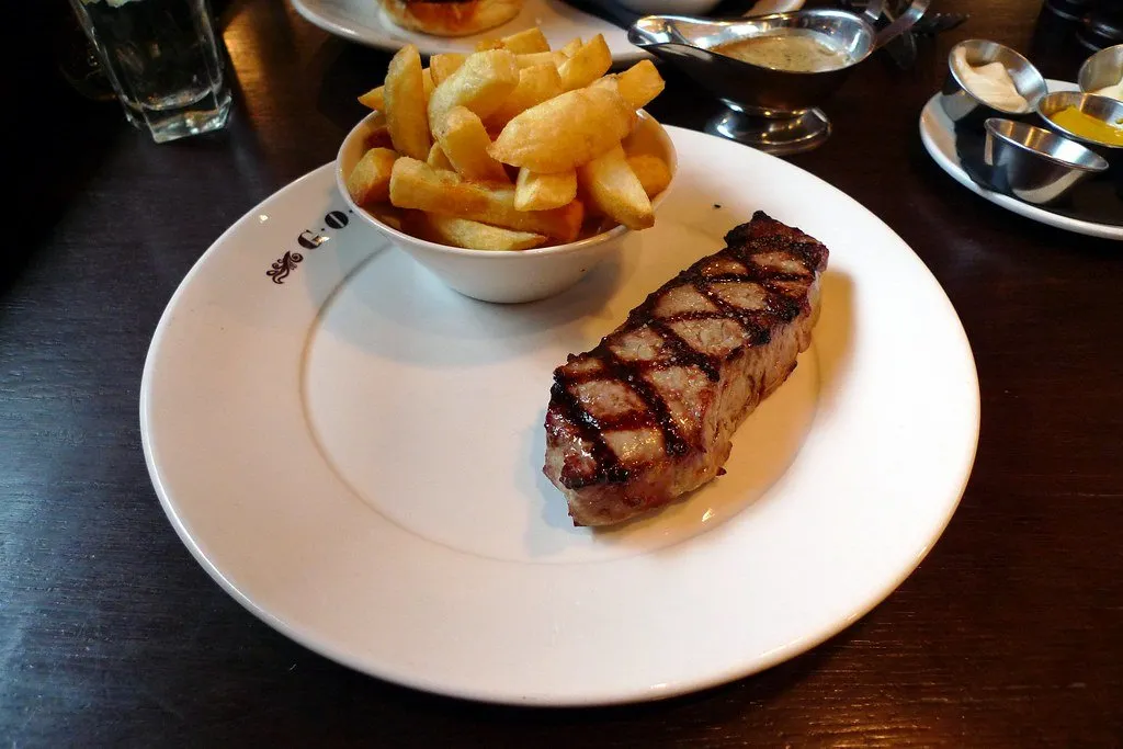 A grilled steak with a bowl of chips