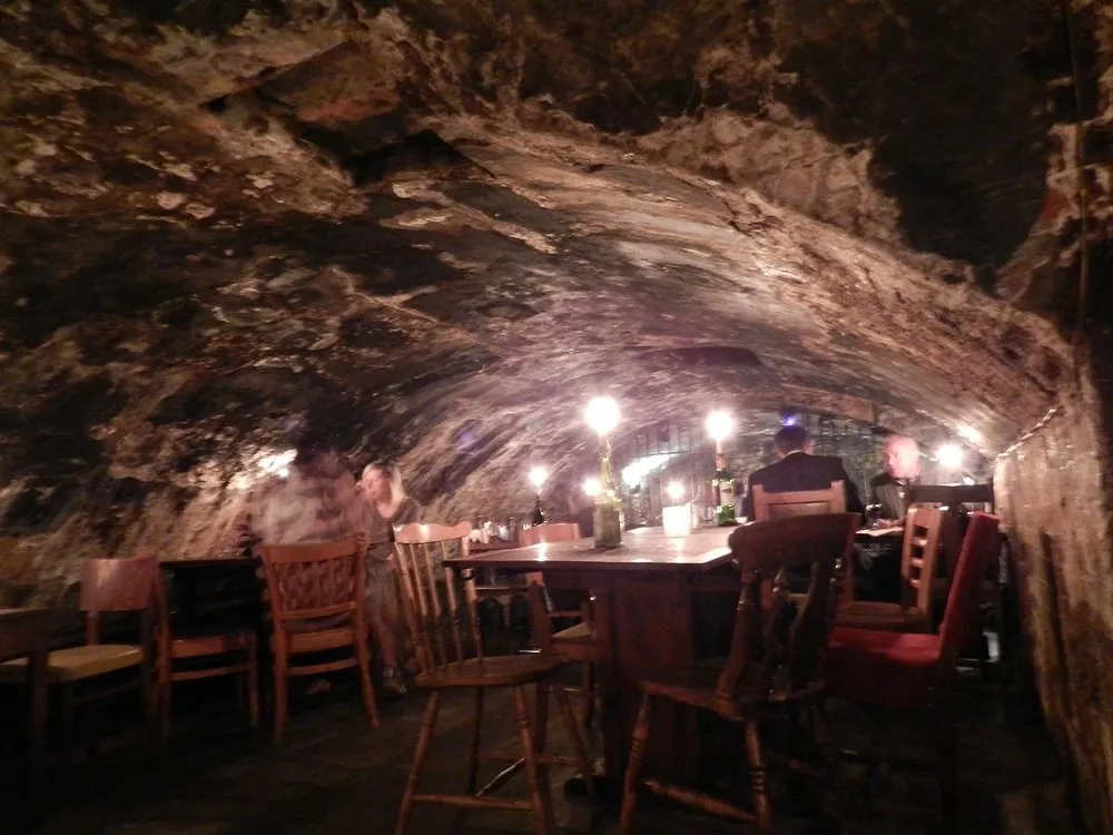 The vaulted candlelit cellar at Gordon's Wine Bar, blackened rough stone ceiling low overhead, candles stuck in bottles on wooden tables with people drinking