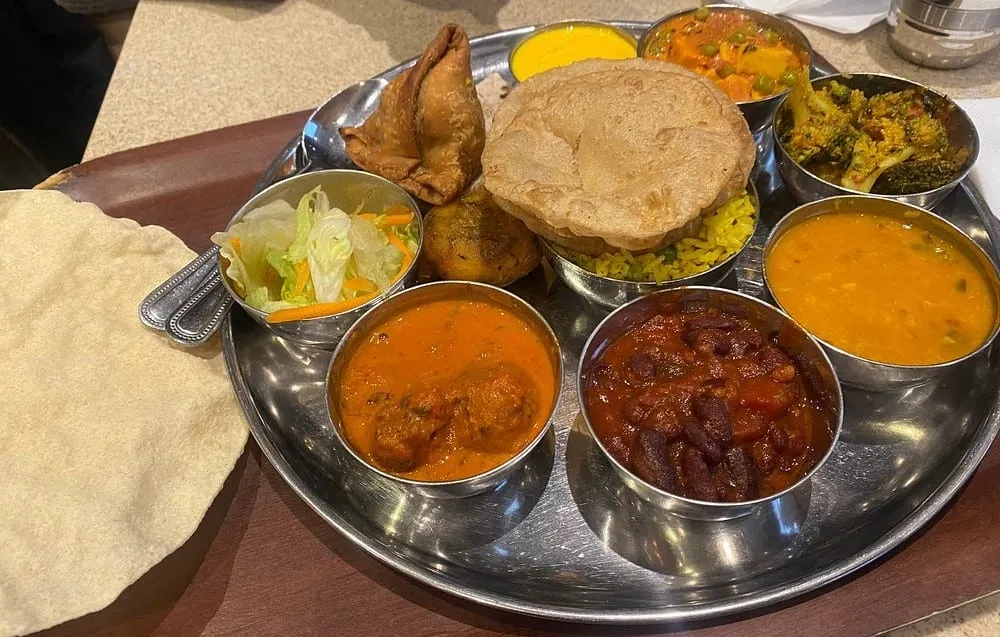 A steel thali tray at Govinda's holding a samosa, puri, dal, rajma, broccoli sabzi, salad and rice, with poppadoms alongside