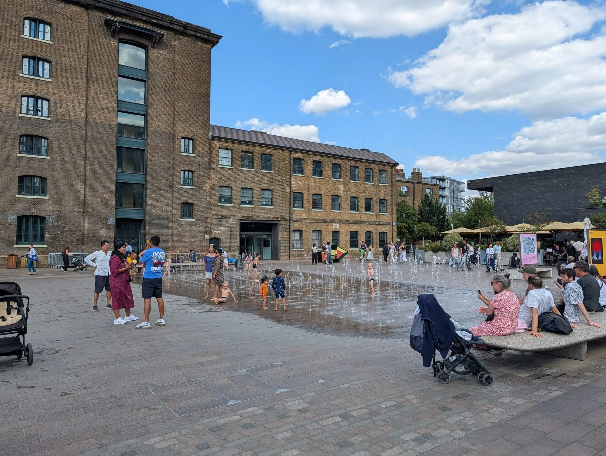Children running through the ground fountains at Granary Square in King's Cross on a summer afternoon