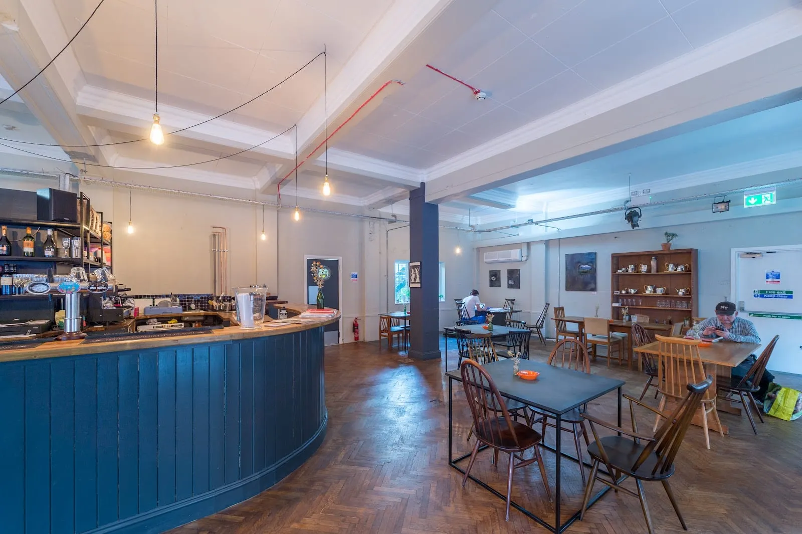 The ground-floor café and bar at Green Rooms, with a curved blue counter, wooden tables and exposed pipework