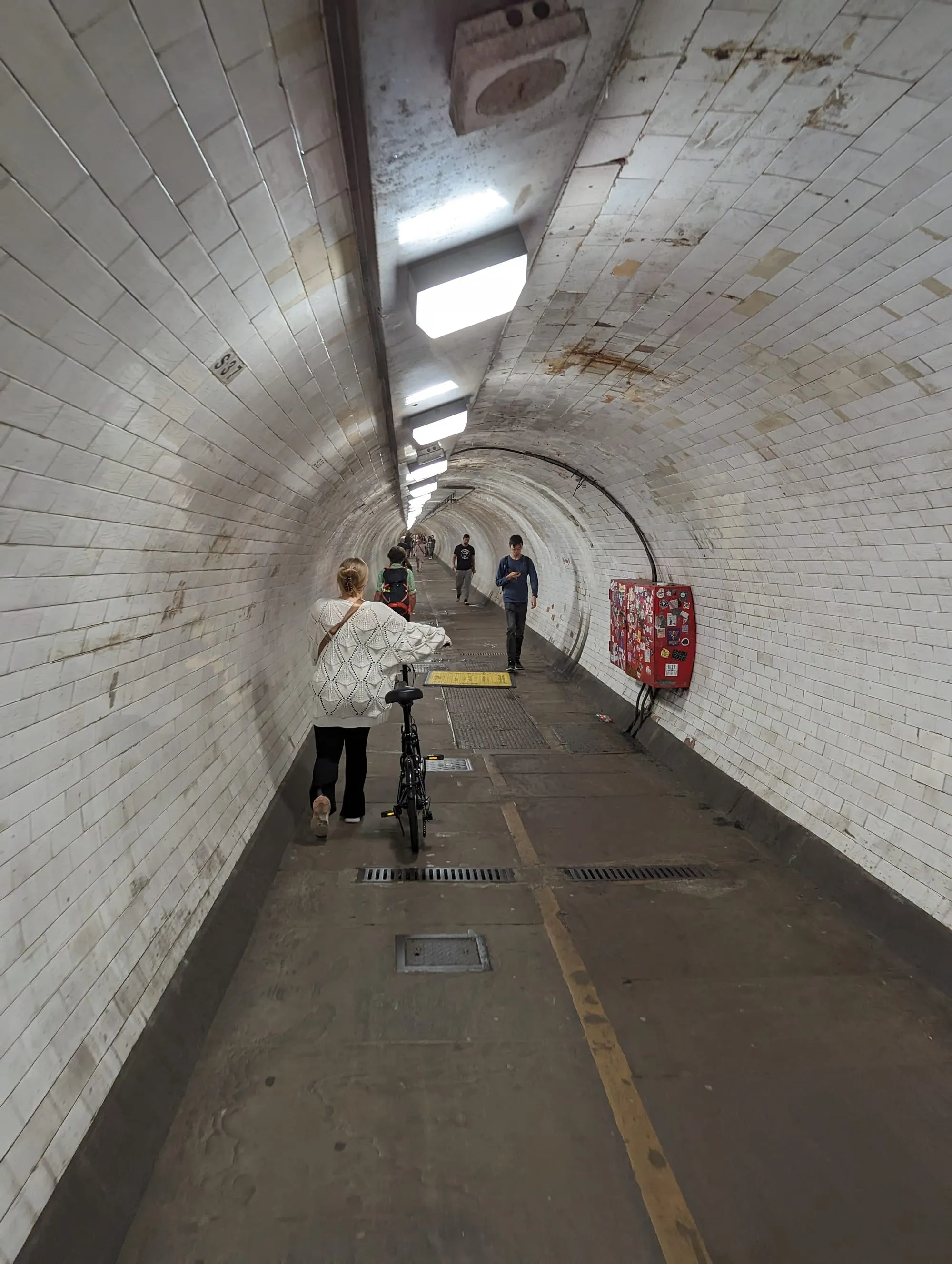 The white-tiled Greenwich Foot Tunnel stretching ahead, with walkers and a yellow line down the floor