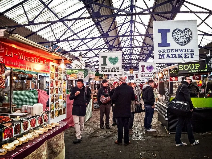 Food stalls under the glass and iron roof of Greenwich Market, with banners reading I Heart Greenwich Market