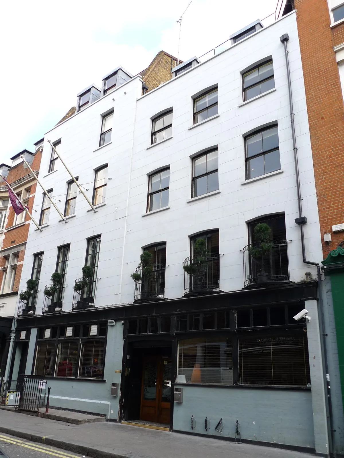 The white-painted front of the Groucho Club on Dean Street, with clipped topiary on the first-floor balconies and a flag over the door