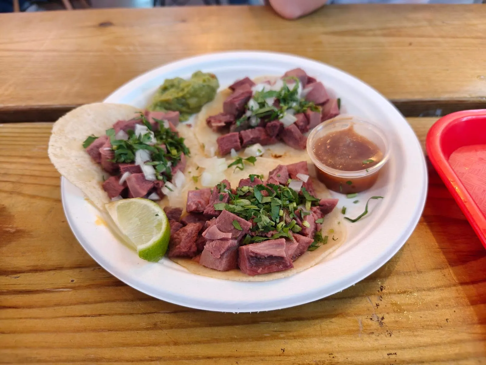 Three birria tacos on a plate with a cup of consomme, guacamole and a lime wedge