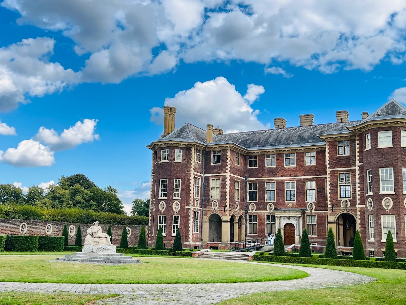 Ham House in Richmond, a red-brick Jacobean mansion with tall chimneys, seen across the garden lawn and its reclining stone statue