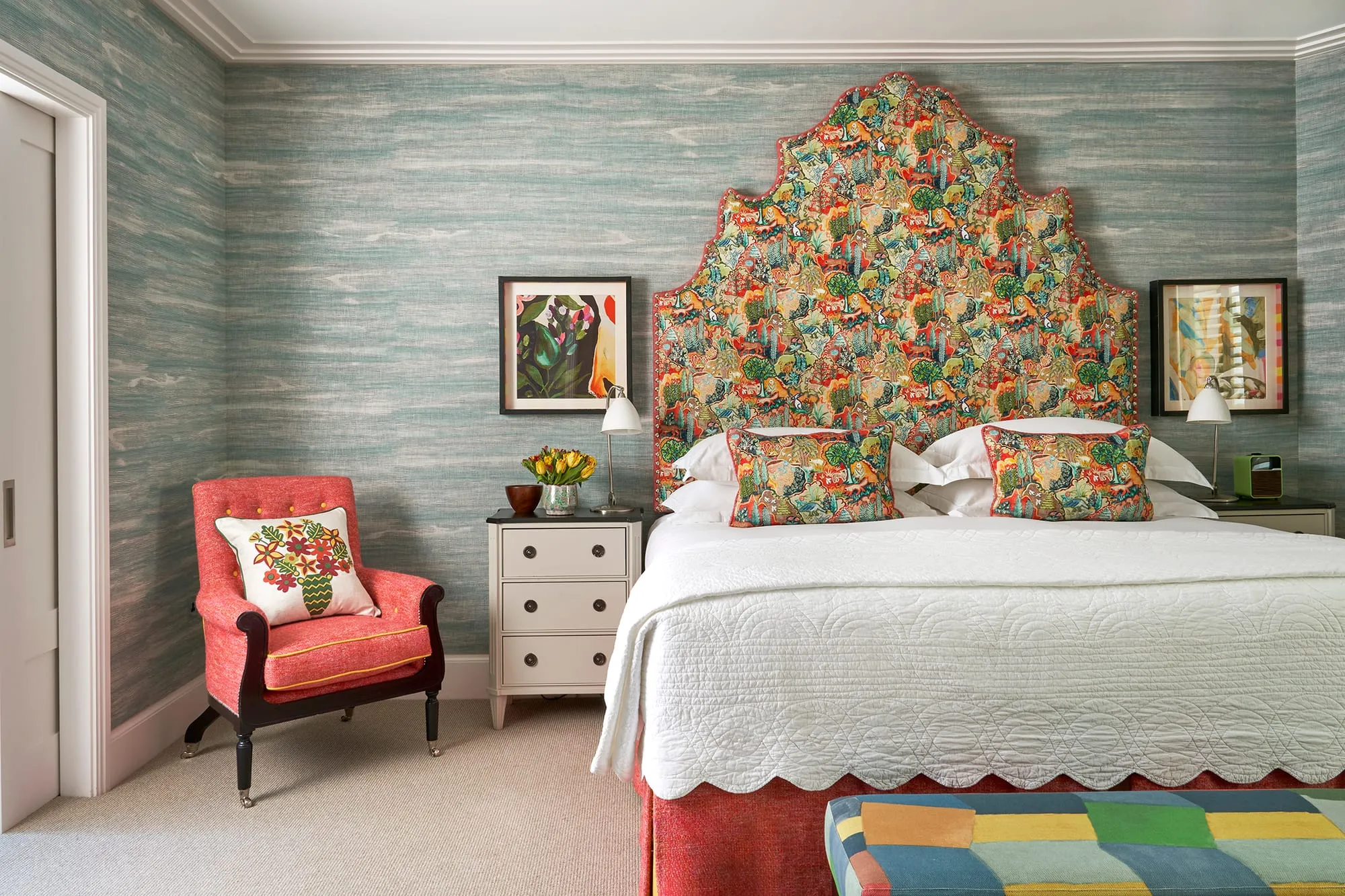 A Ham Yard Hotel bedroom with a brightly patterned forest-scene headboard, cream walls, olive curtains and a mustard armchair