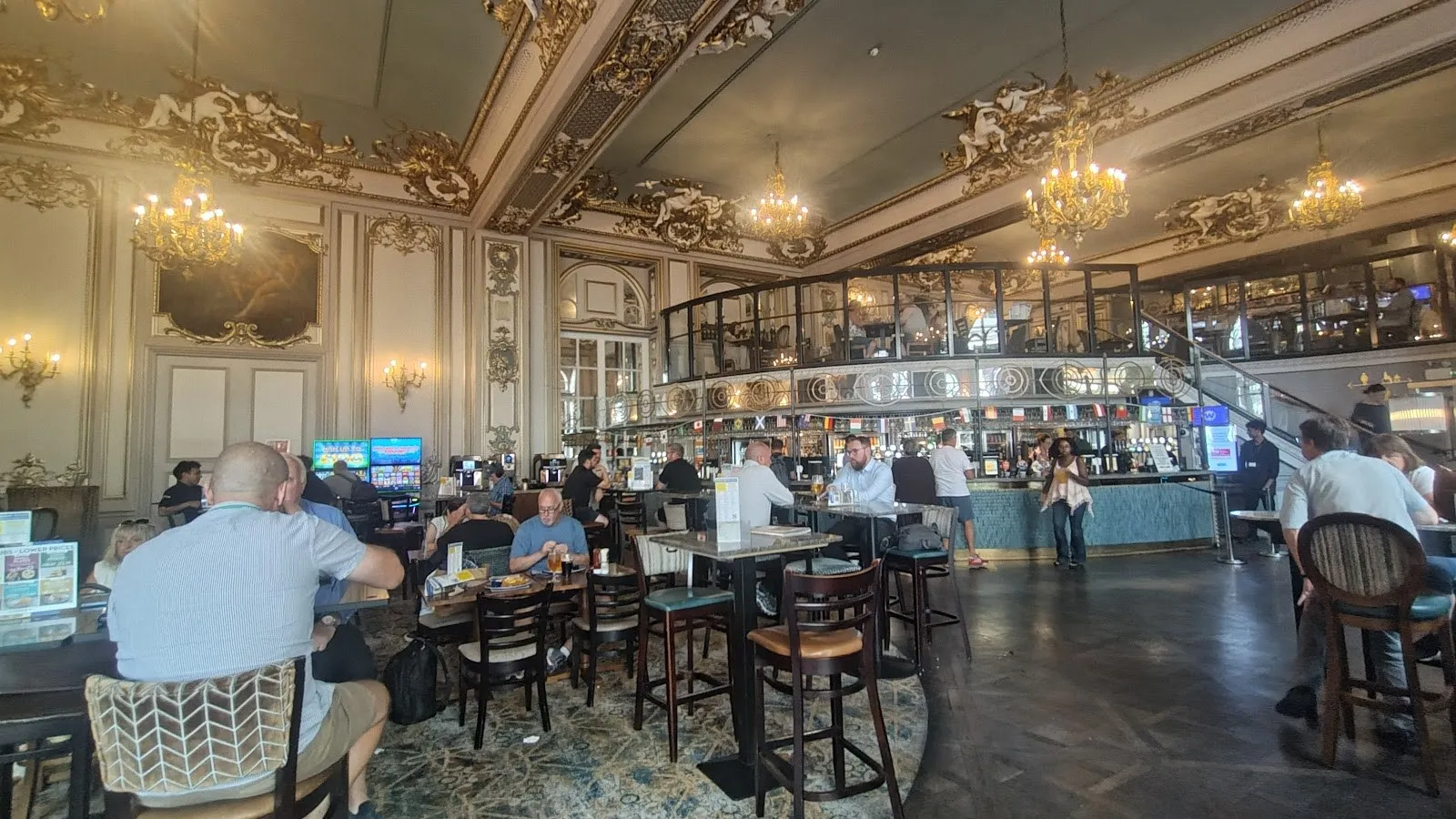 The gilded plasterwork ceiling, chandeliers and mirrors of Hamilton Hall, with the bar below