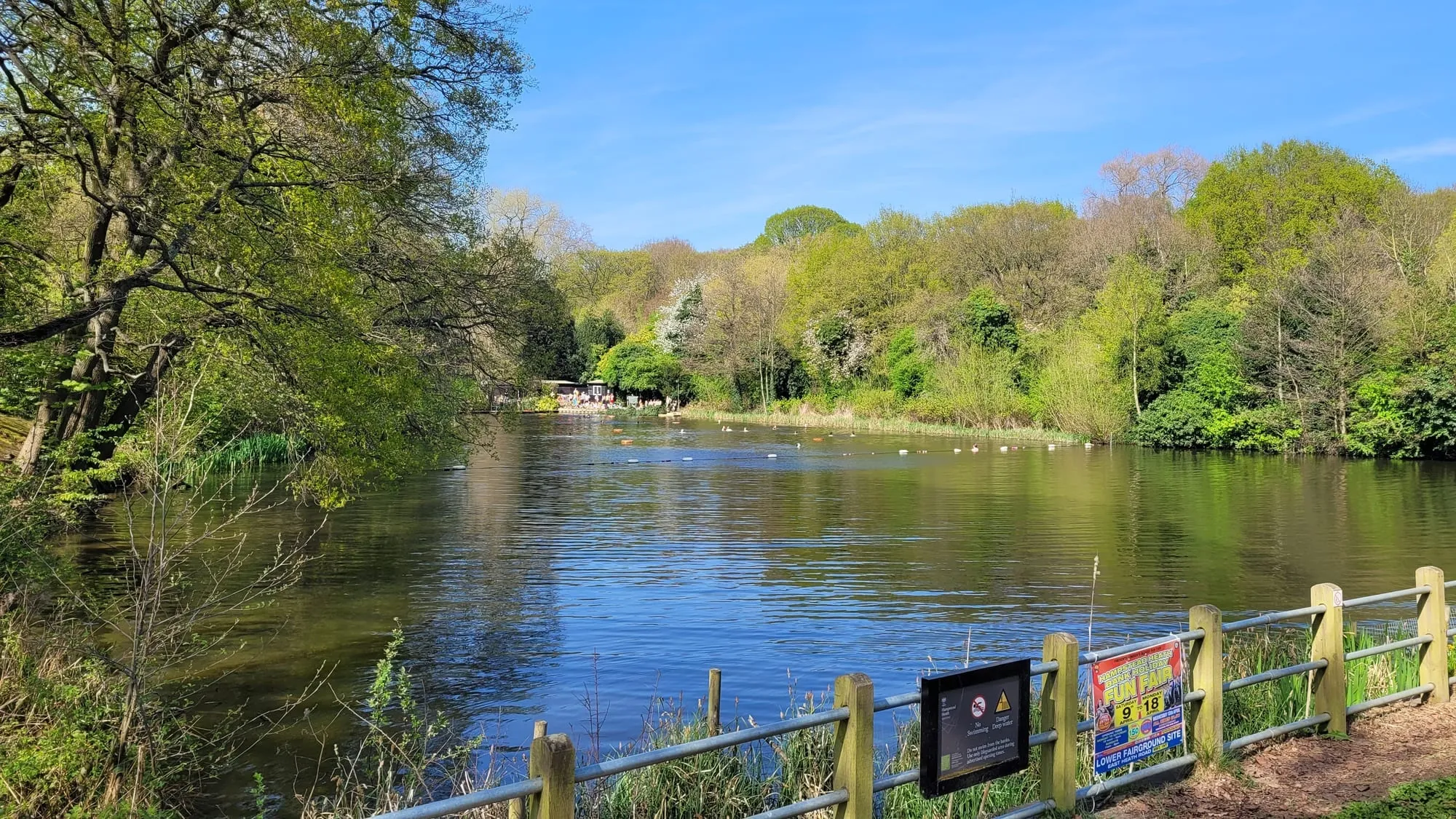 One of the Hampstead Heath bathing ponds, ringed by trees, with a swimmers' noticeboard in the foreground