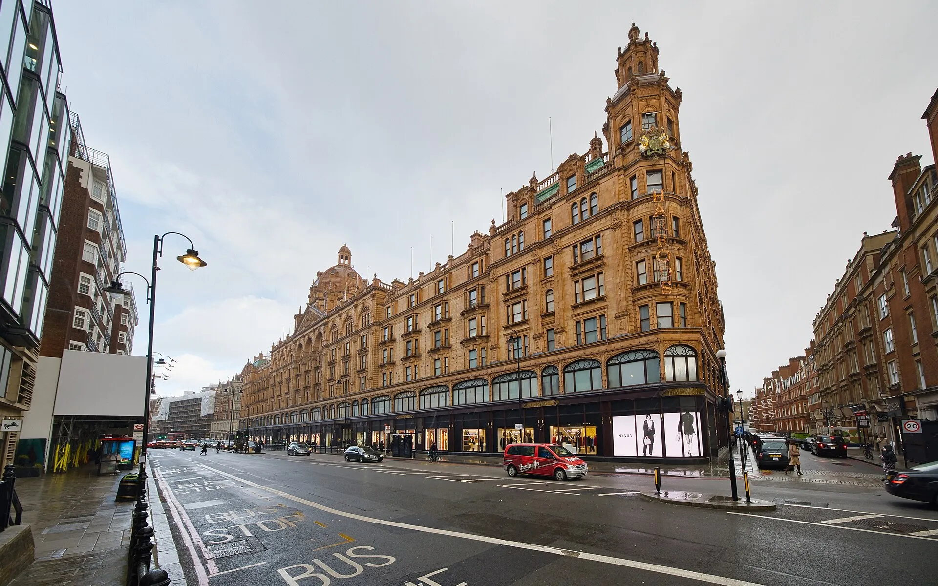 The terracotta facade of Harrods on Brompton Road in Knightsbridge on a wet day, with lit window displays along the ground floor