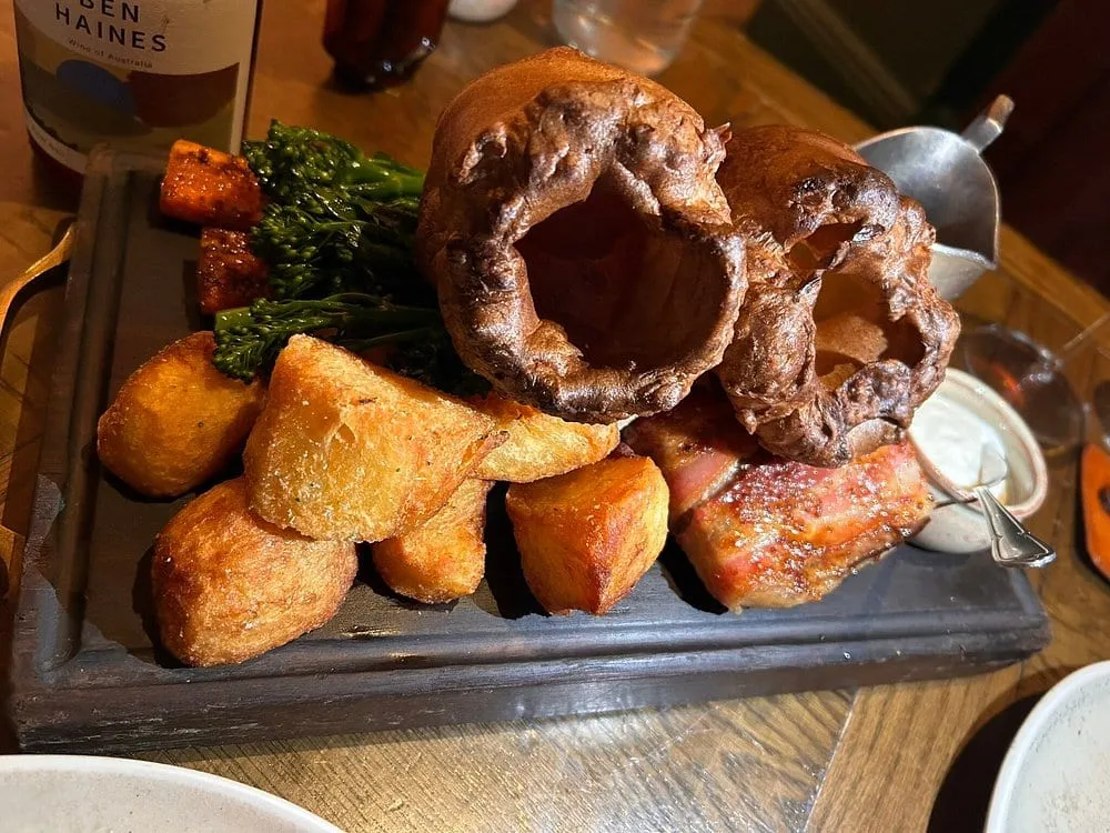 A roast at The Harwood Arms on a wooden board: pink beef, two tall Yorkshire puddings, roast potatoes and broccoli