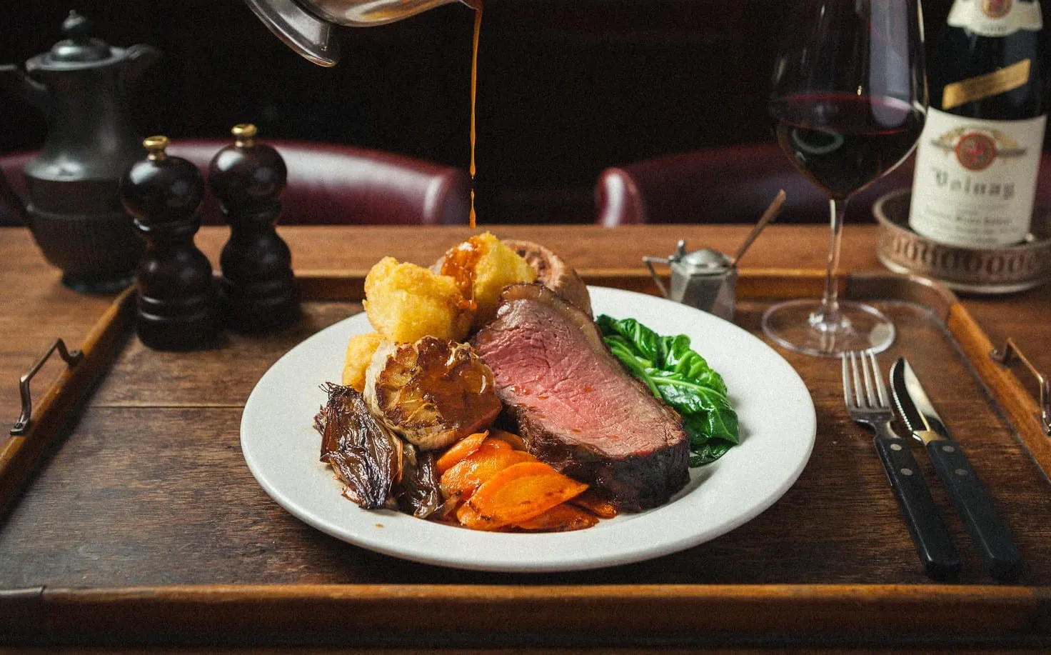 Gravy being poured over a Sunday roast at Hawksmoor: beef, a Yorkshire pudding, roast potatoes, glazed carrots and greens