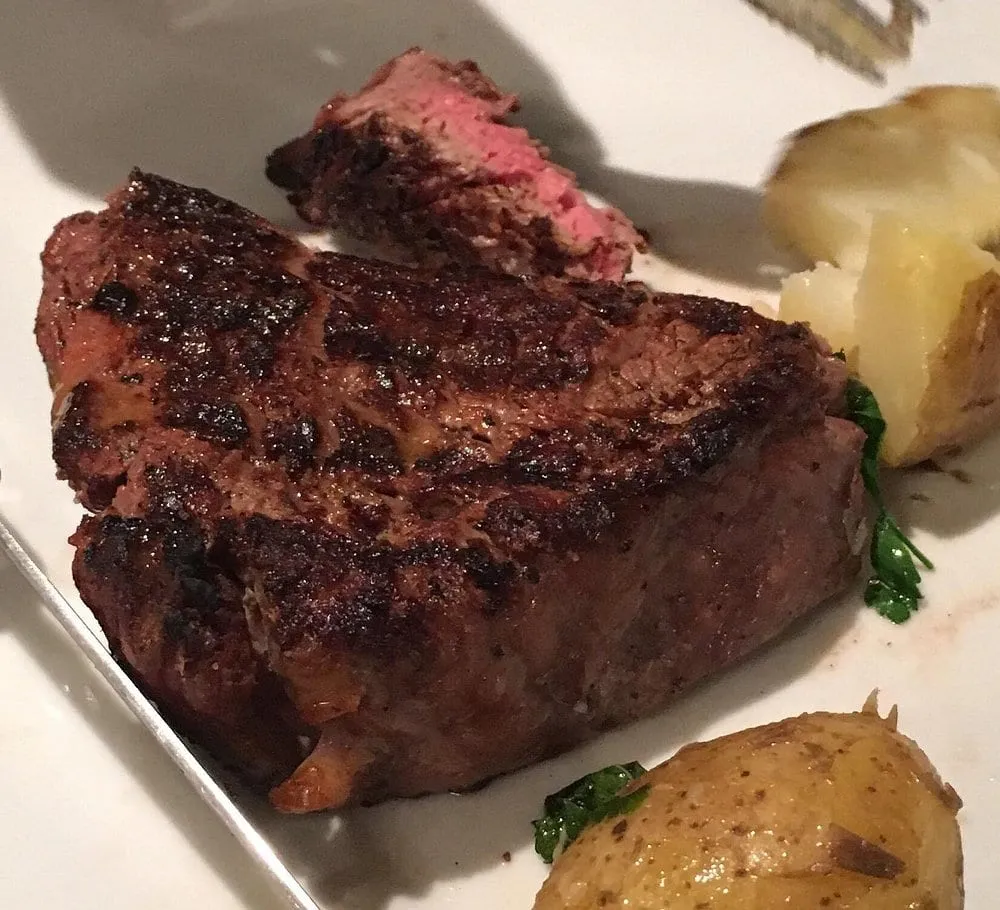 A thick grilled steak at Hawksmoor, dark and crusted from the charcoal with a pink centre showing in the sliced end, served with crushed potatoes