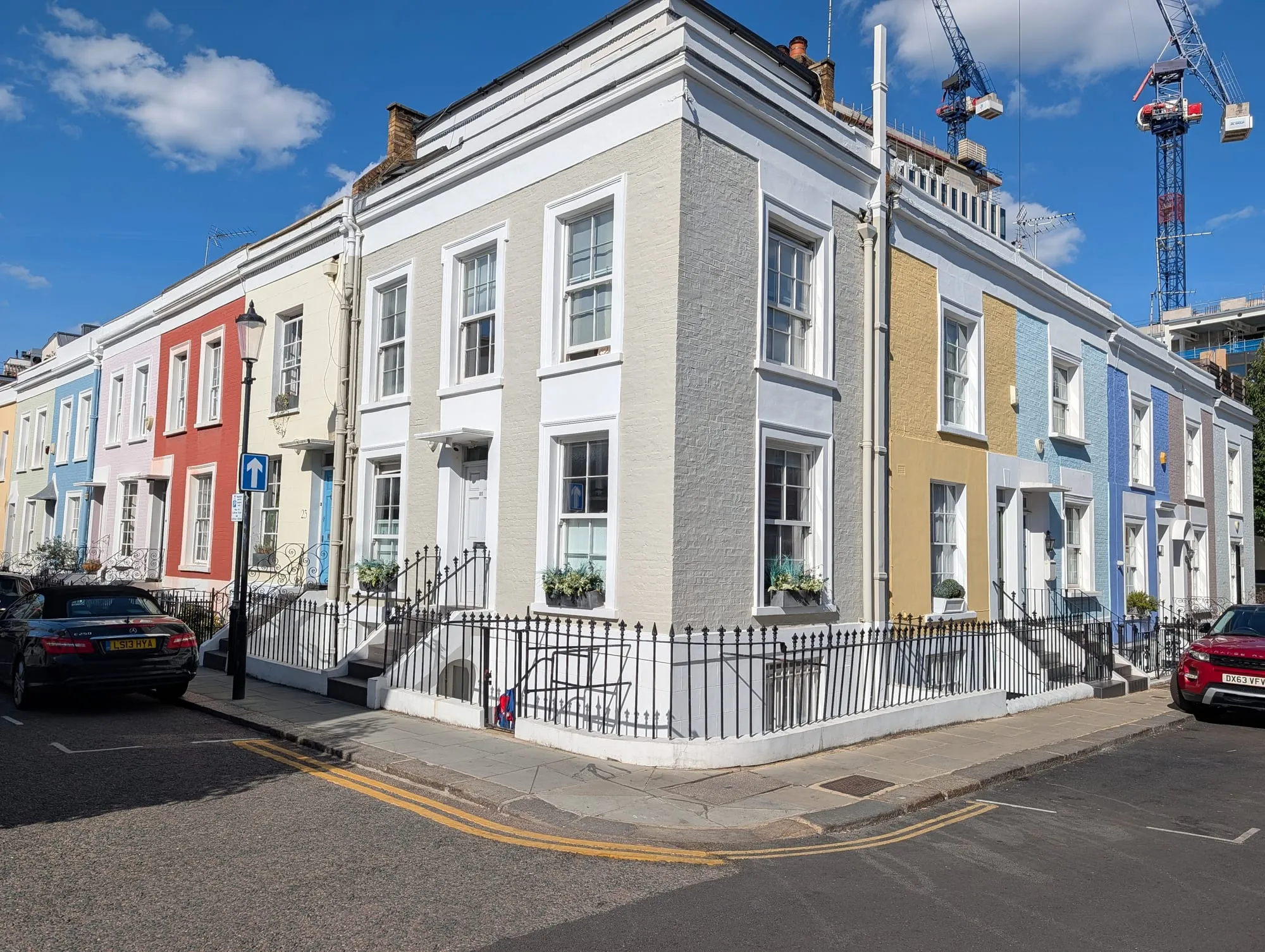 A corner terrace of small houses on Hillgate Place painted pale blue, red, cream and yellow under a clear sky