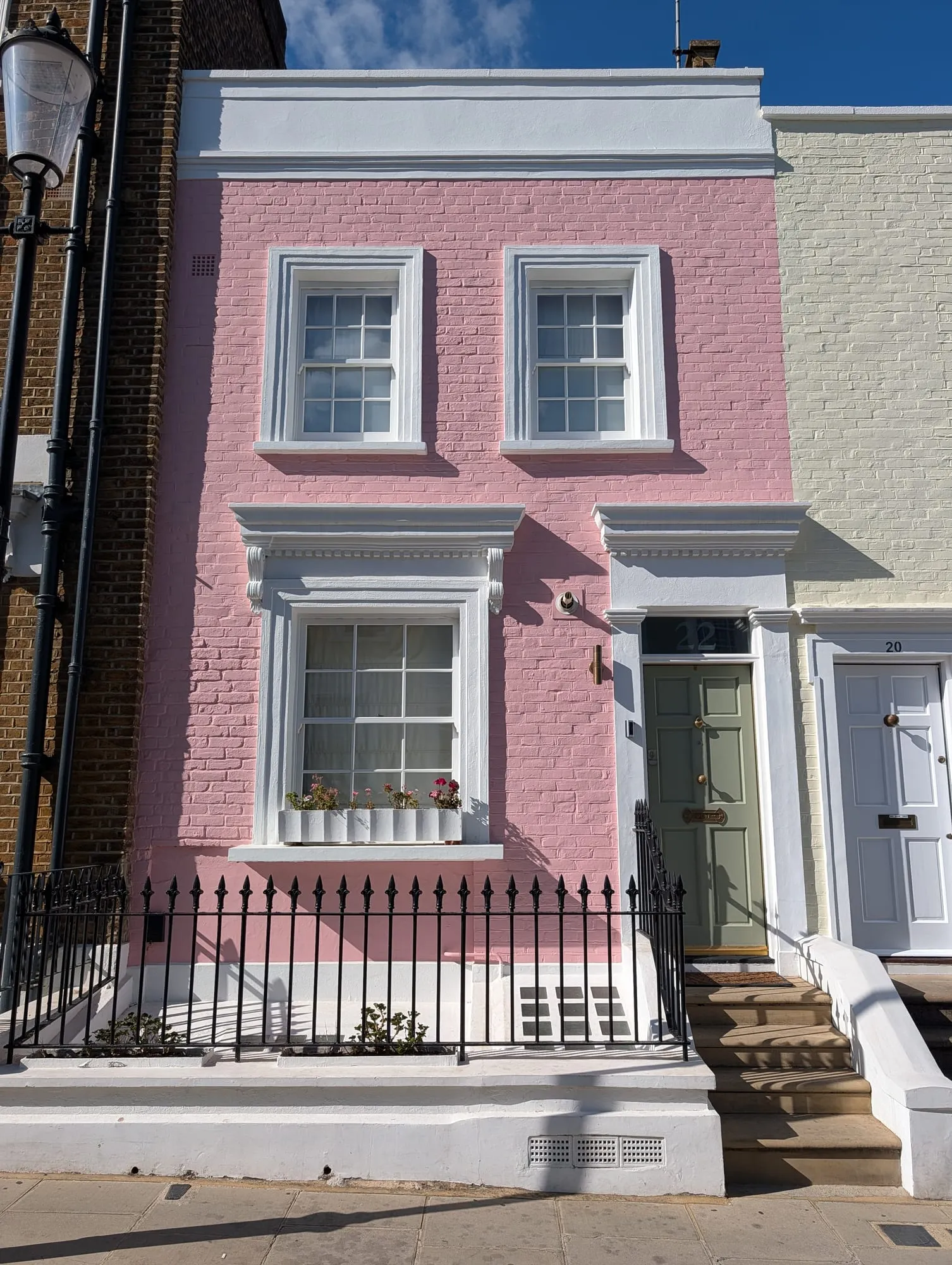 A pink house on Hillgate Place with white sash windows and a sage green front door