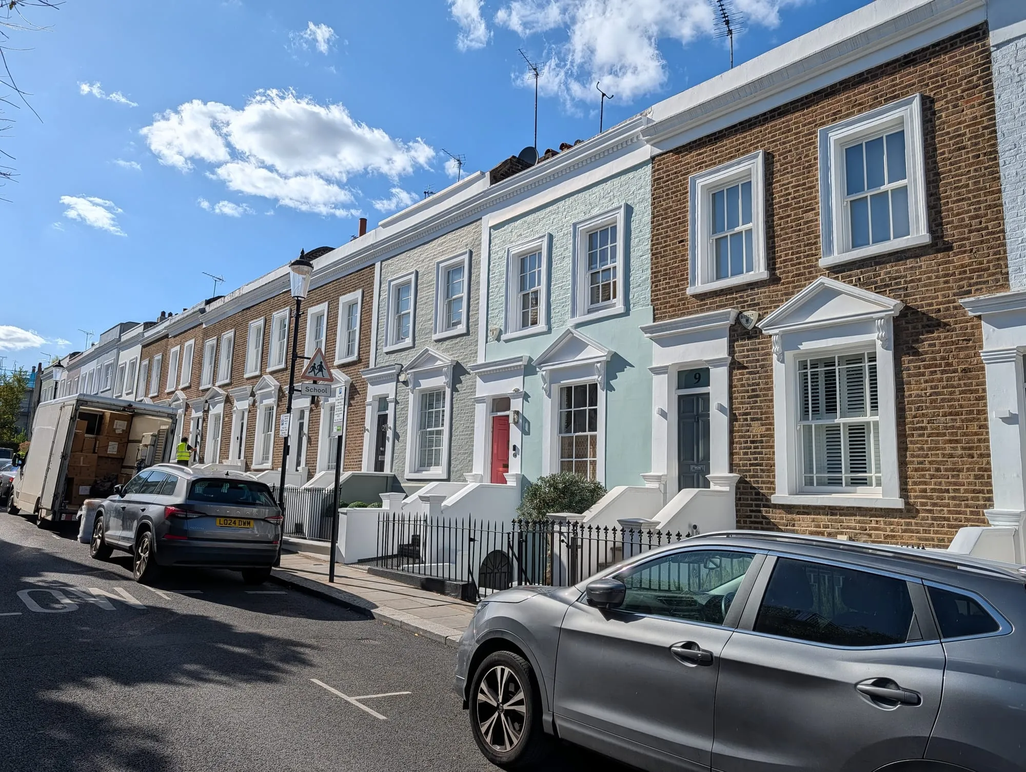 A row of pale blue, grey and cream houses along Hillgate Place, seen down the length of the street