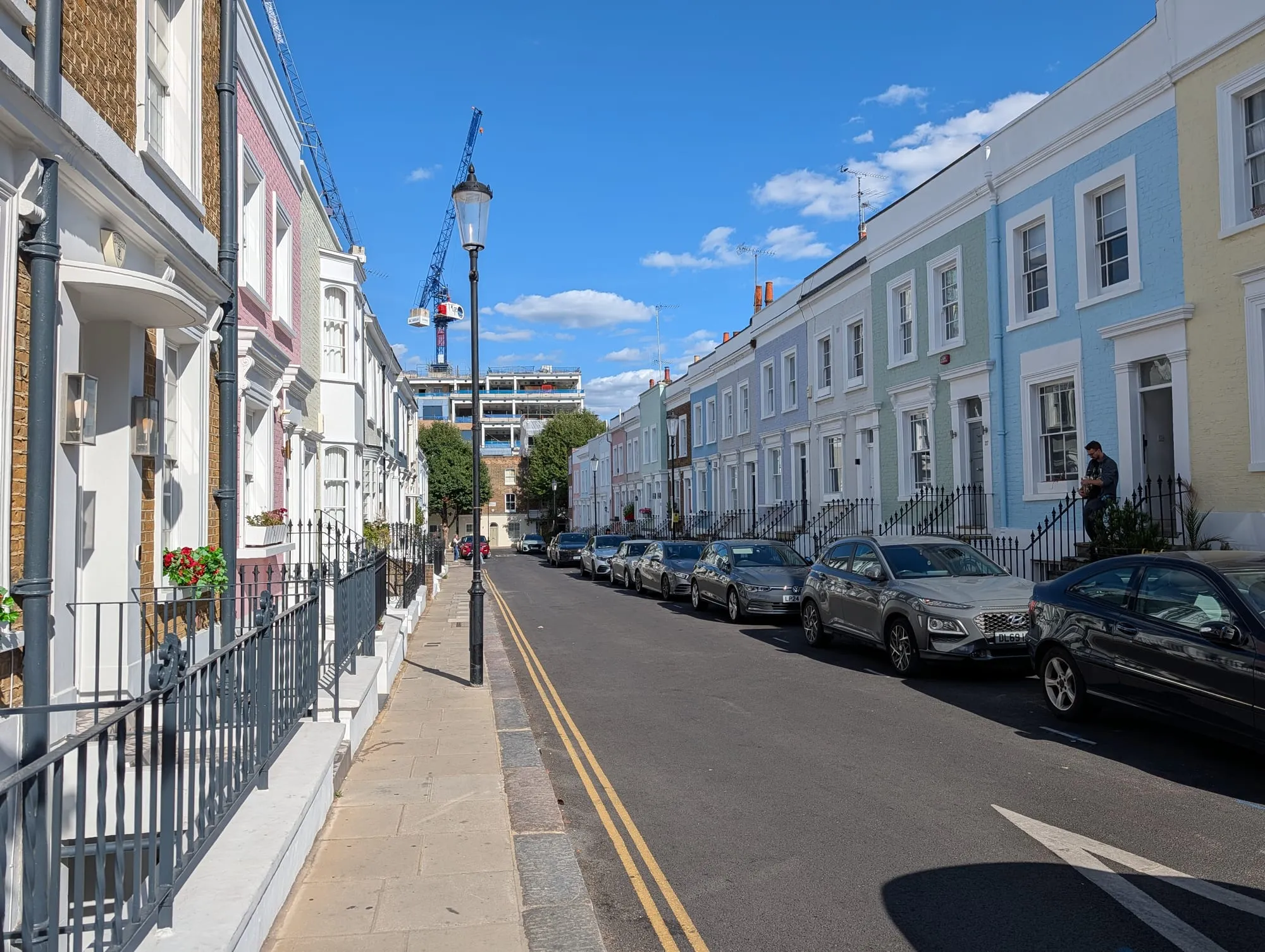 Looking down Hillgate Street past a row of pastel-painted terraced houses towards a crane on the skyline