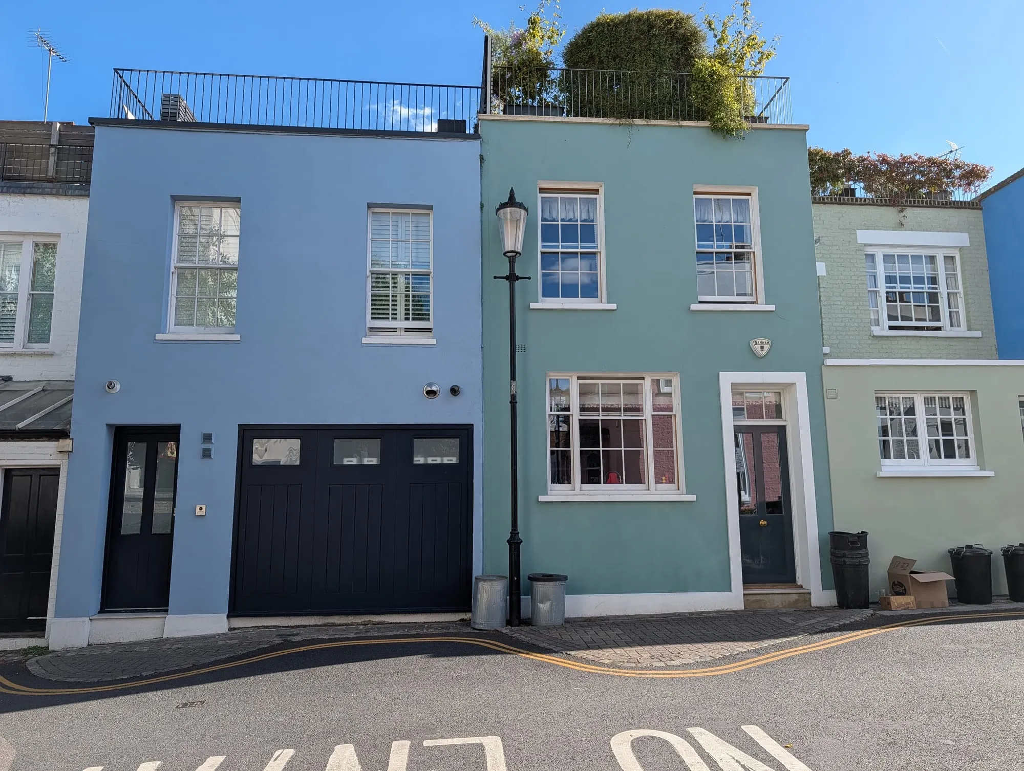 Two small houses in Hillgate Village, one painted powder blue and one pale green, with white sash windows