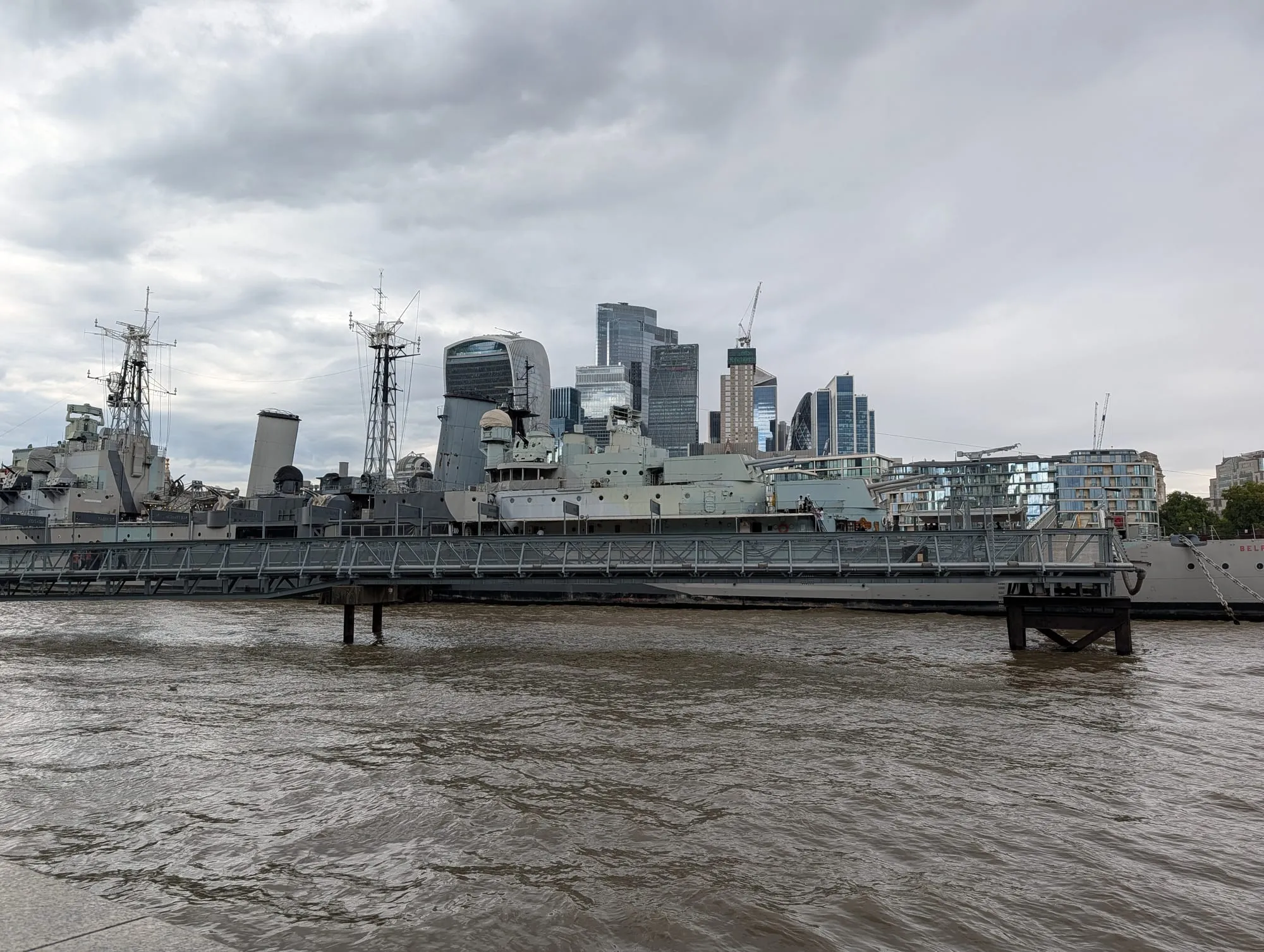 HMS Belfast moored on the Thames with the City of London's towers rising on the far bank
