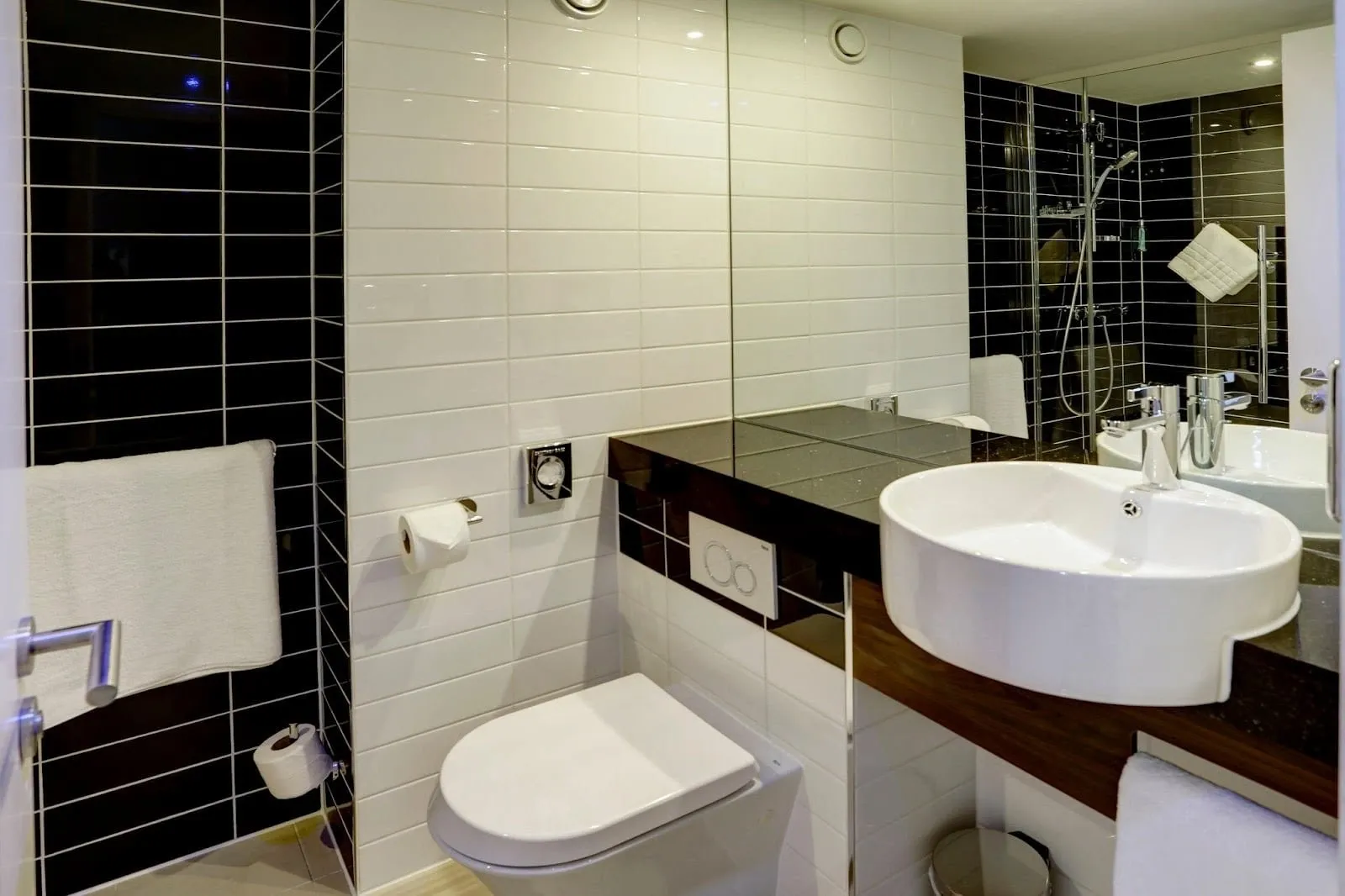 The bathroom at Holiday Inn Express London – ExCeL, with a round basin, a wall-hung toilet and a shower behind black tiles