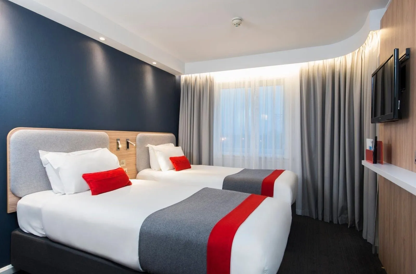 A twin room at Holiday Inn Express London – Greenwich with a blue feature wall and red and grey bed runners