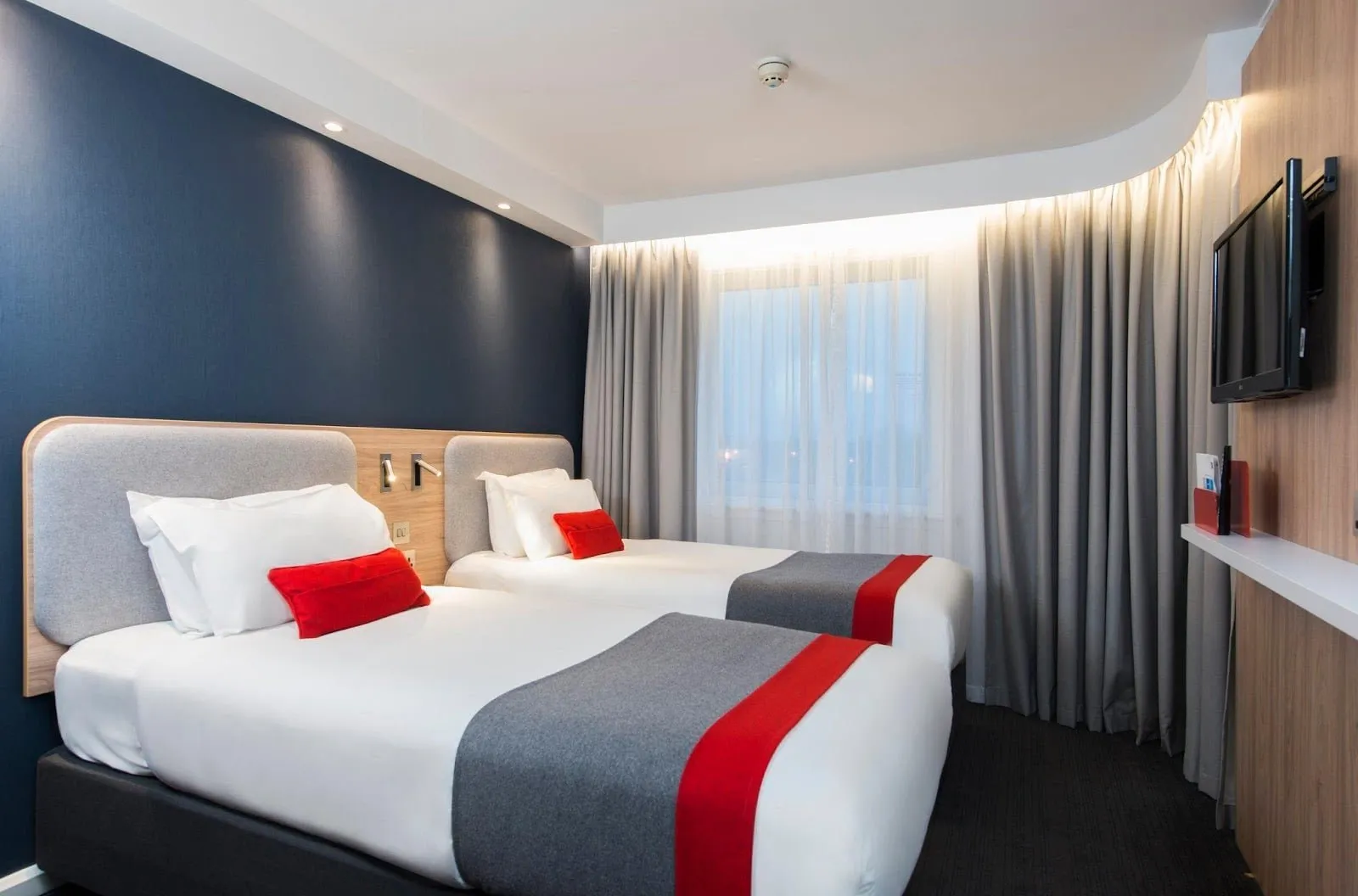 A twin room at Holiday Inn Express London – Greenwich with a blue feature wall and red and grey bed runners