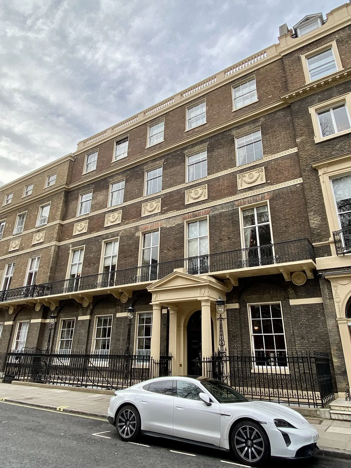 The brick Georgian front of Home House on Portman Square, with a pedimented porch, iron balconies and railings, and a white car parked outside