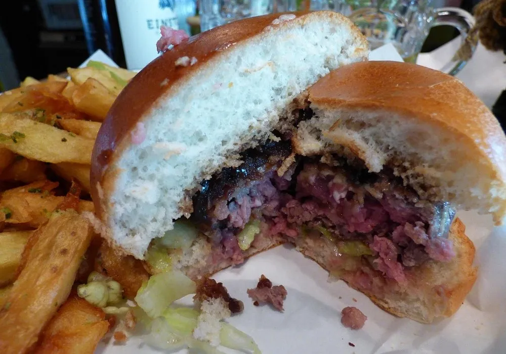 A burger cut in half showing a coarsely ground patty cooked pink, beside a pile of thick-cut chips