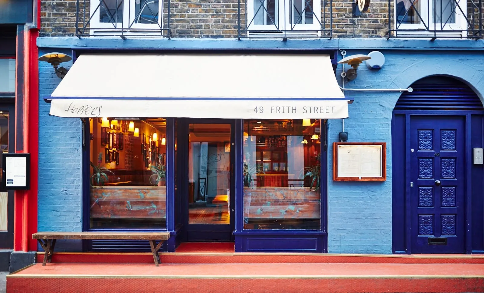 The blue-painted shopfront of Hoppers at 49 Frith Street in Soho, with a cream awning and a menu case beside the door