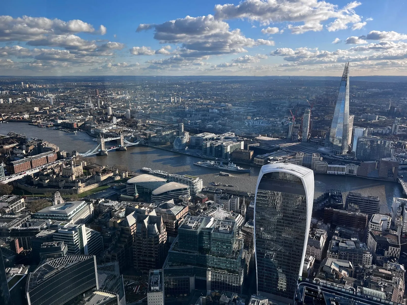 The view east from a high City viewing floor: the Thames curving past Tower Bridge and the Tower of London, with the Walkie-Talkie in the foreground and The Shard beyond