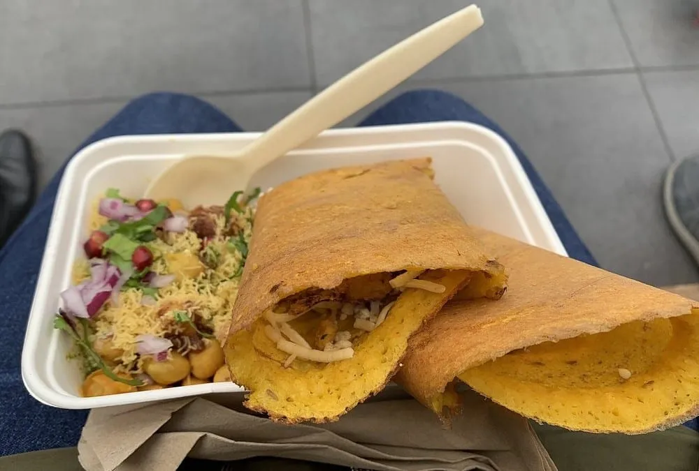 A takeaway tray at Borough Market holding a folded dosa and a portion of chaat topped with sev, pomegranate and red onion