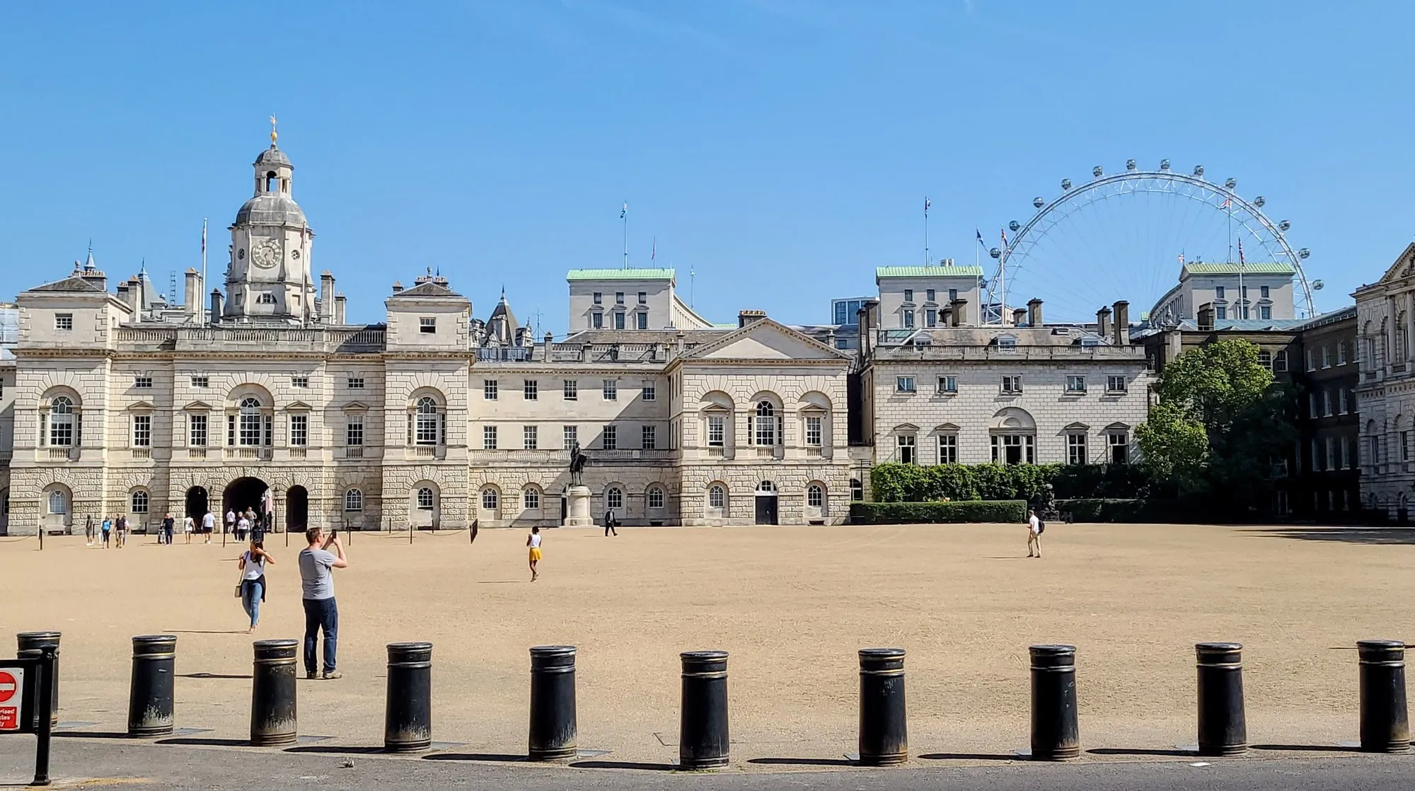 The Horse Guards building on a quiet afternoon, with tourists on the parade ground and the London Eye visible behind