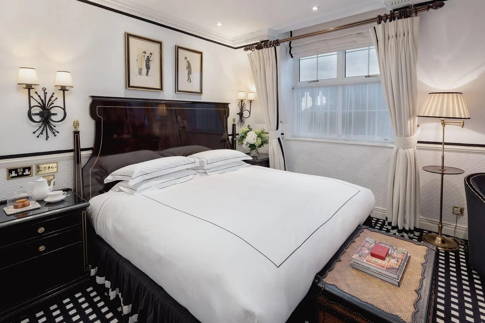 A double room at Hotel 41 with a black lacquered headboard, black-and-white check carpet, white curtains edged in black and two framed caricatures of top-hatted gentlemen