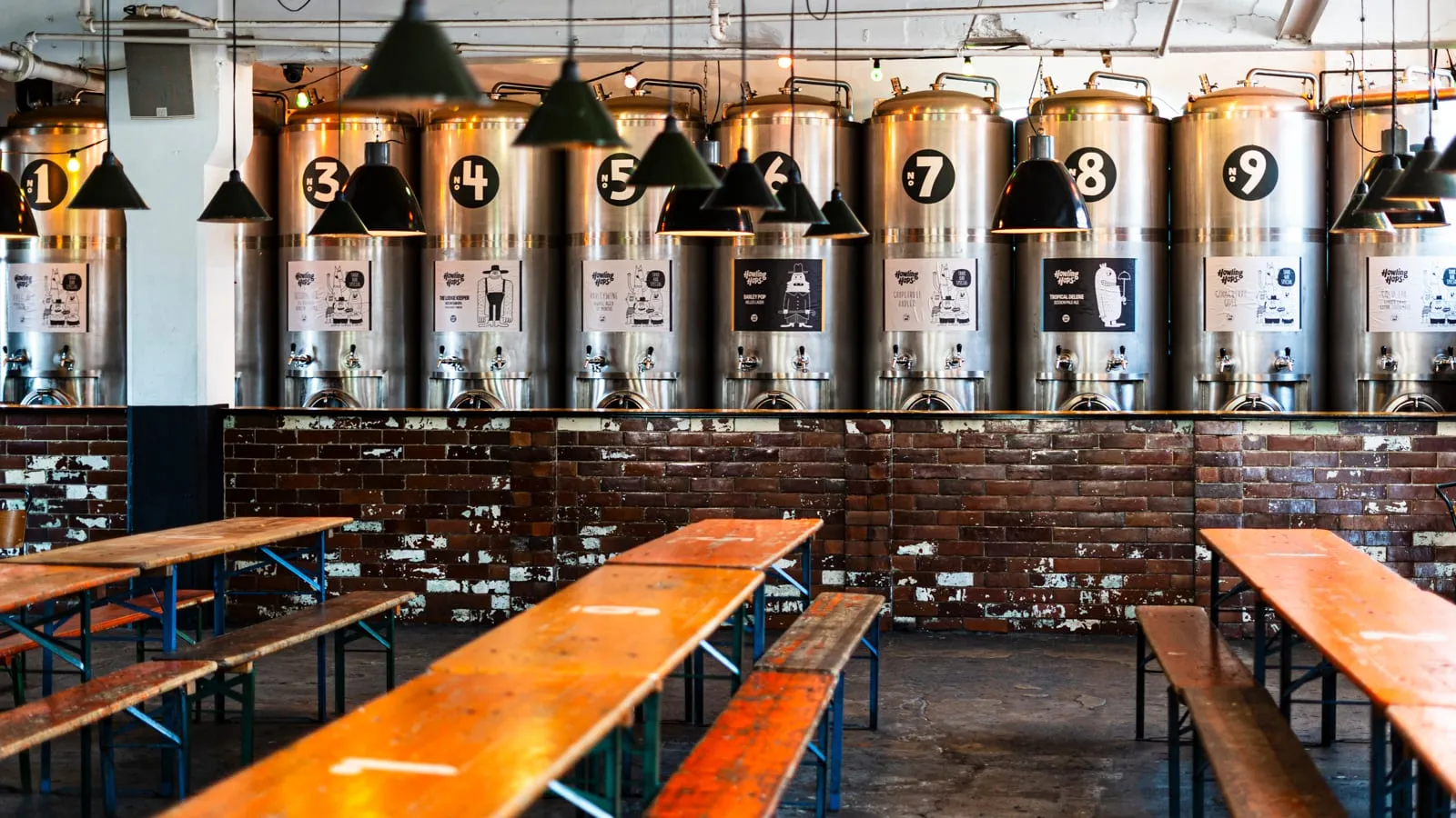 A row of numbered steel tanks at Howling Hops, each with its own tap, beside long wooden bench tables