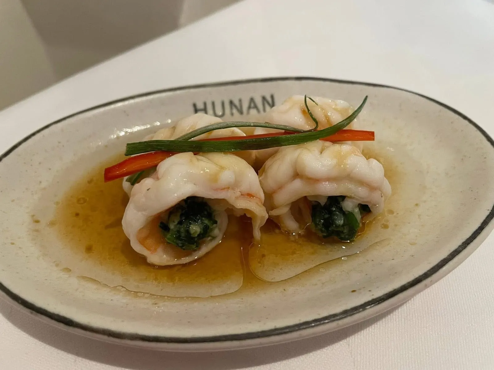 Two stuffed king prawns wrapped around a herb filling, on a white plate marked Hunan