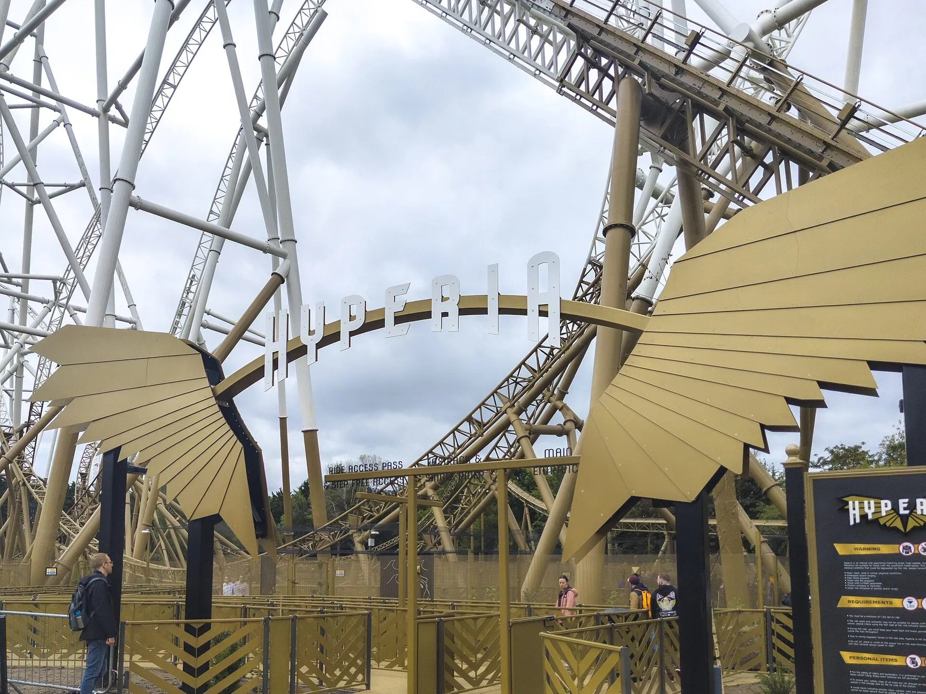 The entrance arch to Hyperia at Thorpe Park, gold metal wings either side of the ride's name, with the white and gold coaster track rising behind