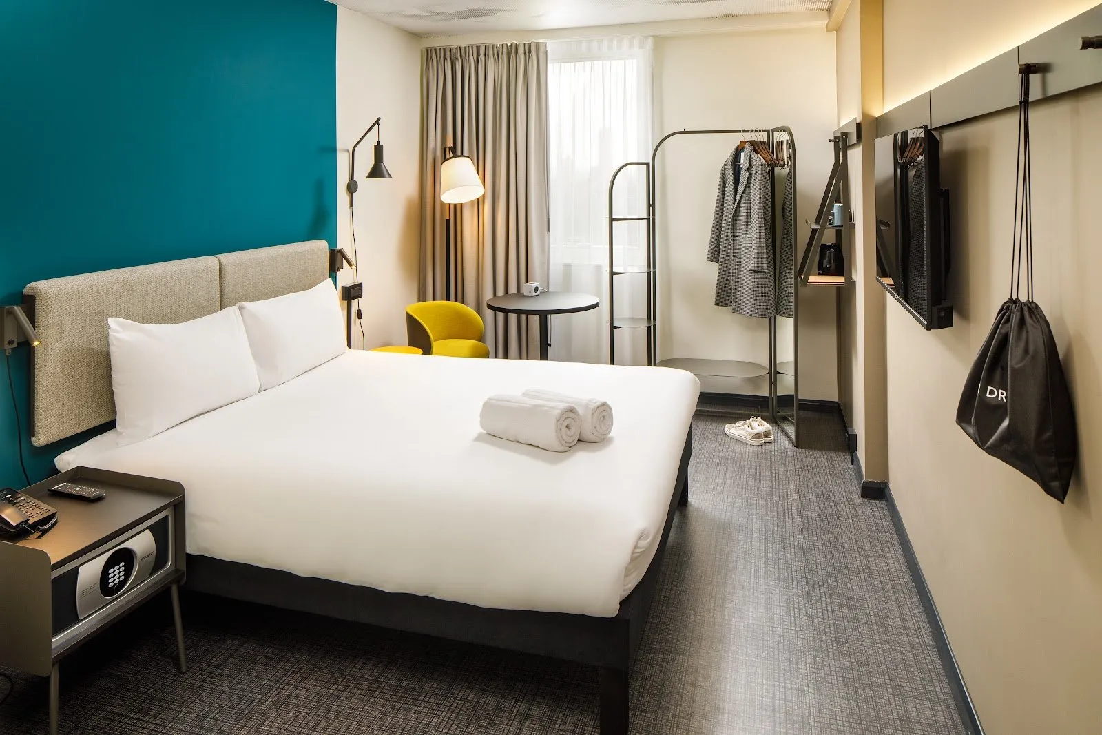 A room at ibis London Blackfriars with a teal accent wall, an open clothes rail and a patterned carpet floor