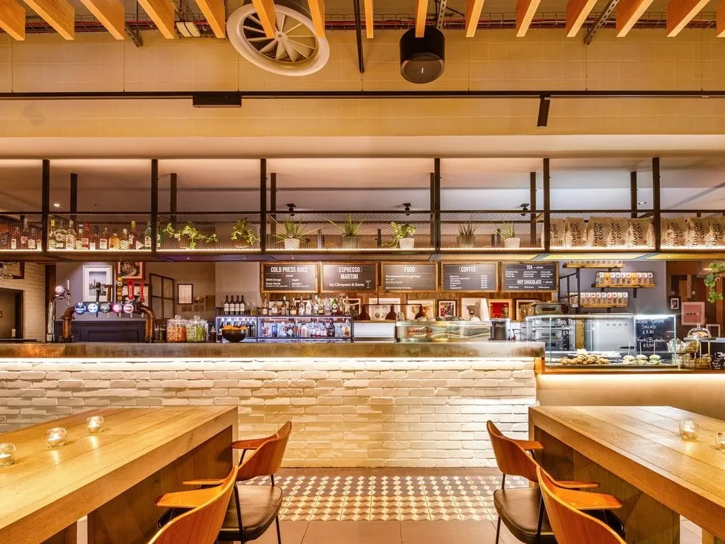 The café-bar at ibis London Canning Town, with menu boards, bar stools and long wooden tables