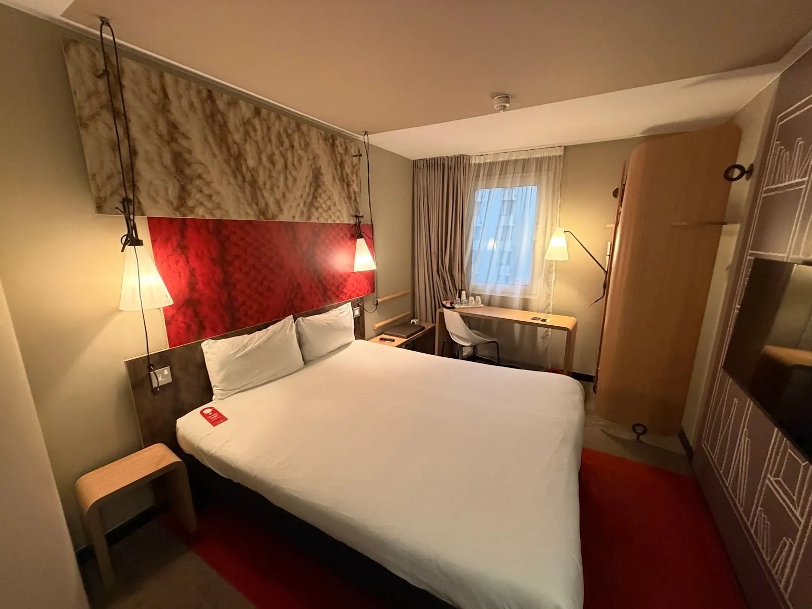 A double room at ibis London ExCeL Docklands with a red headboard panel, a red carpet and a desk by the window