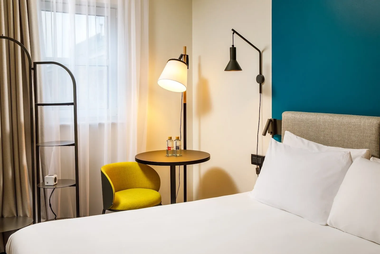 A double room at ibis London Greenwich with a teal wall, a yellow armchair and a round table by the window