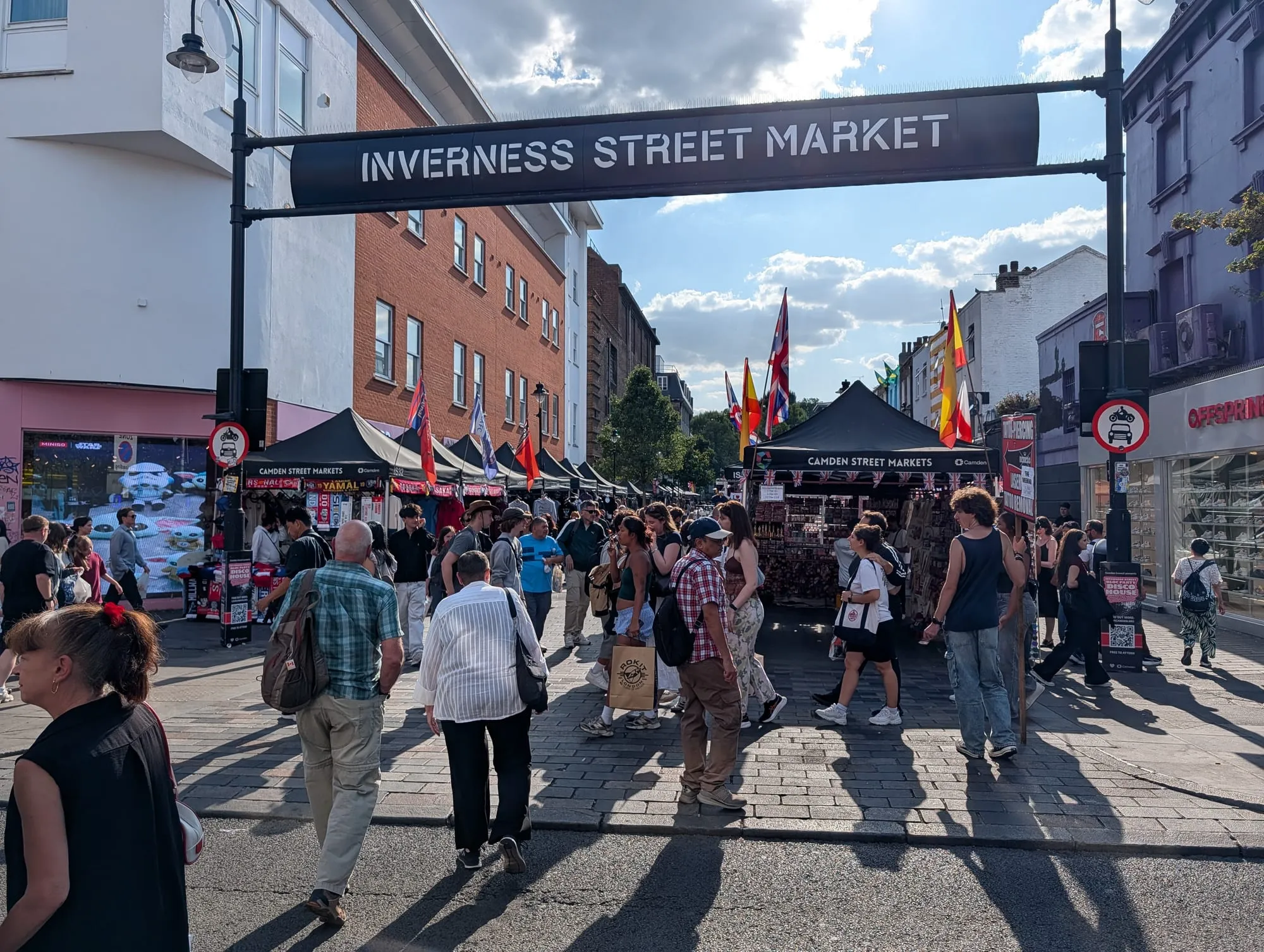 The Inverness Street Market sign spanning the road above a busy street market in Camden