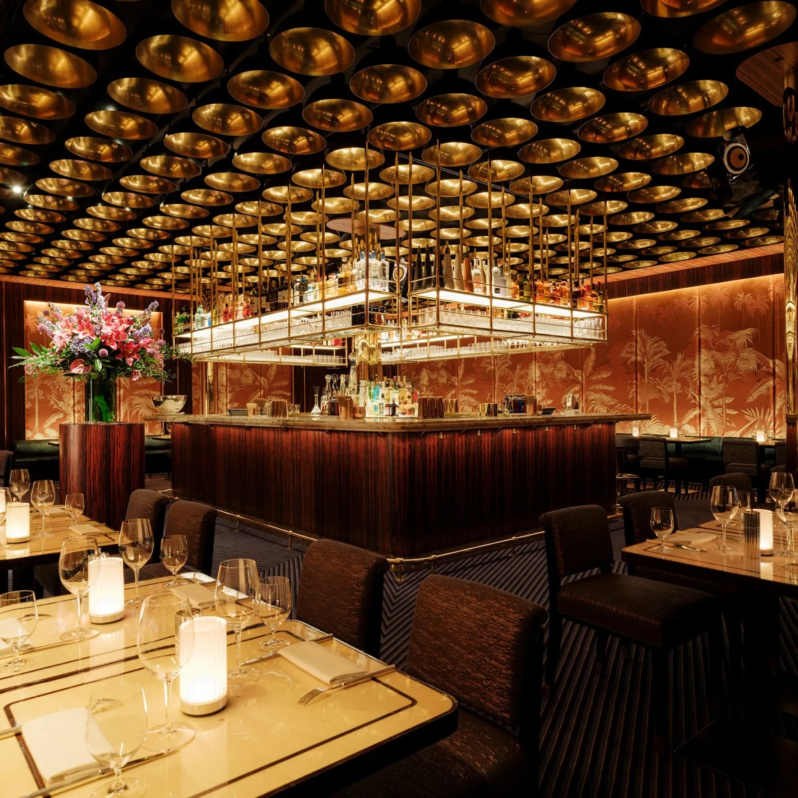 The dining room at Isabel, a ceiling of gold dishes over a long wooden bar, flower arrangements and candlelit tables