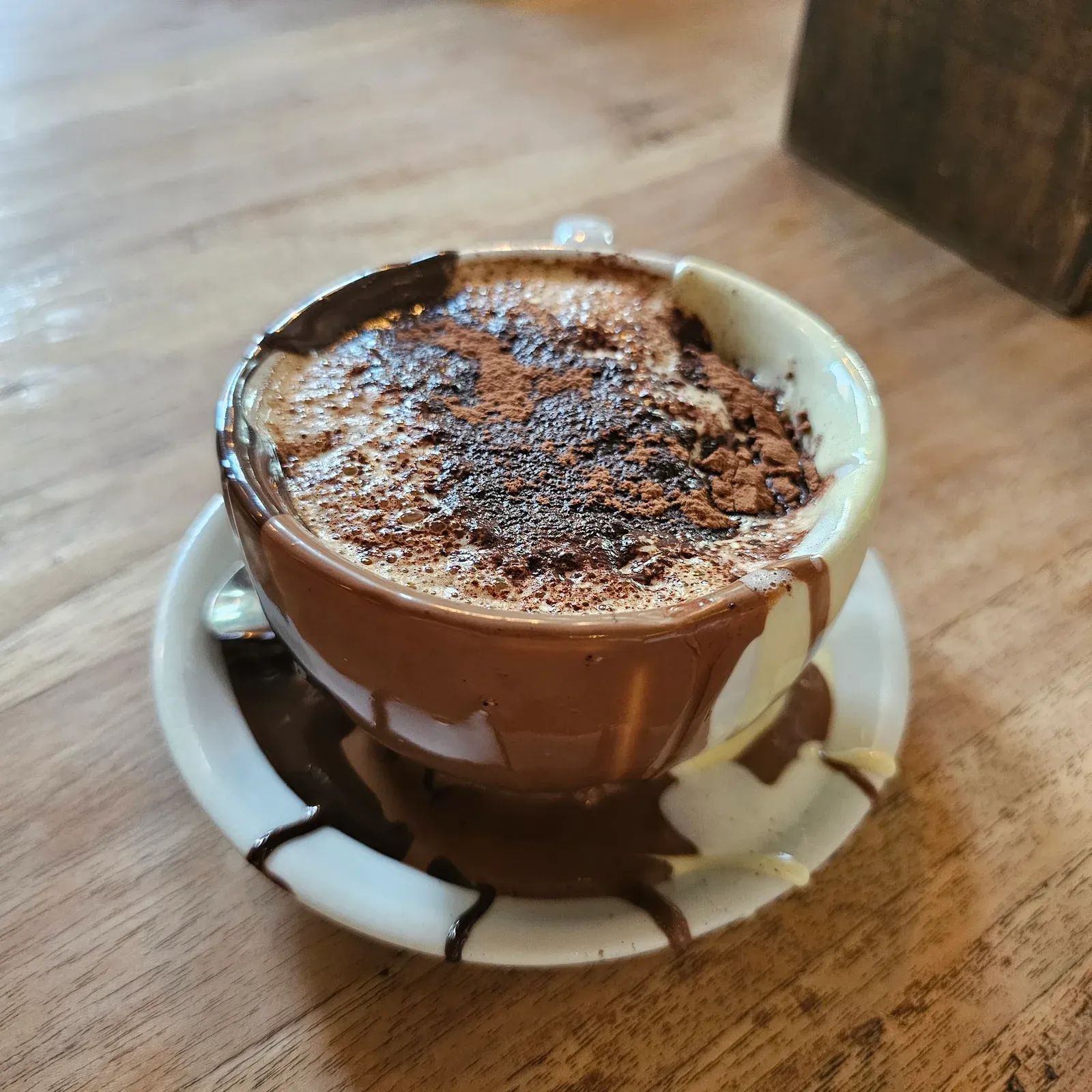 A cup of thick Italian hot chocolate dusted with cocoa, the cup lined with melted chocolate that has run down the outside and pooled on the saucer
