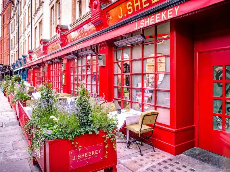 J Sheekey's red-framed shopfront on a Covent Garden side street, with outdoor tables set among potted plants.