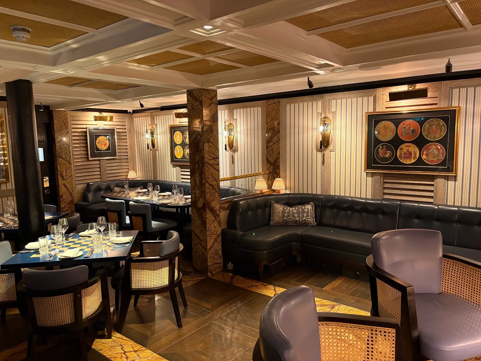 The dining room at Jamavar in Mayfair with dark leather banquettes, marble columns, cane-backed chairs and framed Indian artwork