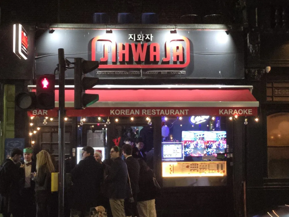 Jihwaja at night, its sign in Korean and English over a red awning reading Bar, Korean Restaurant, Karaoke, with people on the pavement outside