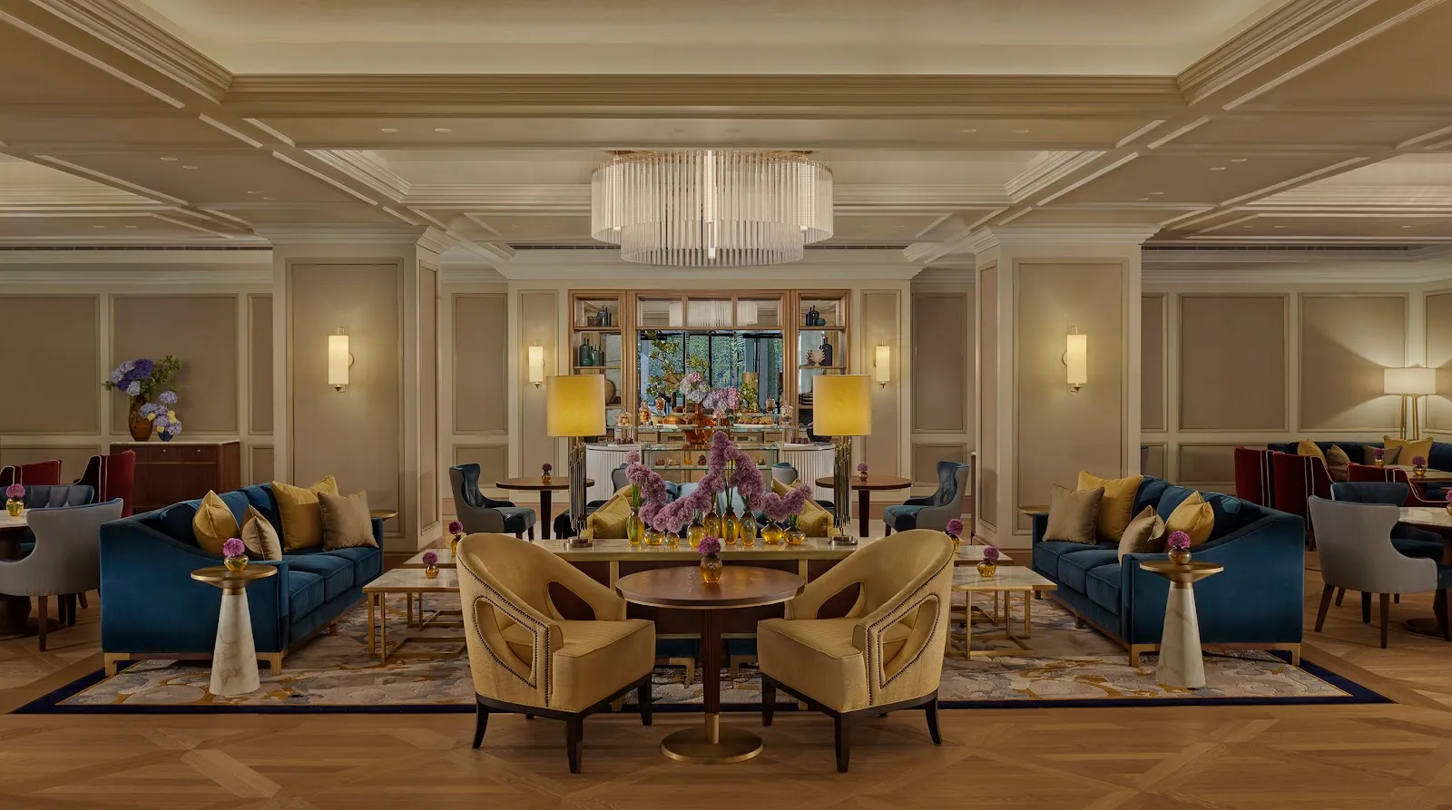 The Chinoiserie lounge at the Jumeirah Carlton Tower: a wide, symmetrical ground-floor room with blue velvet sofas, yellow armchairs and a long pastry counter at the far end