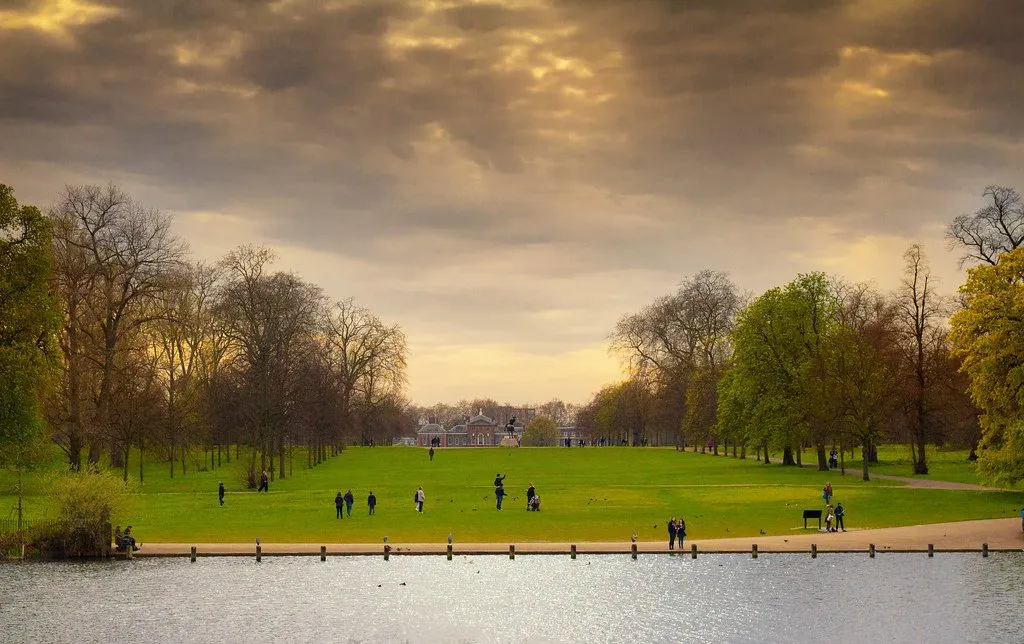 The Round Pond in Kensington Gardens at dusk, with Kensington Palace low on the horizon beyond