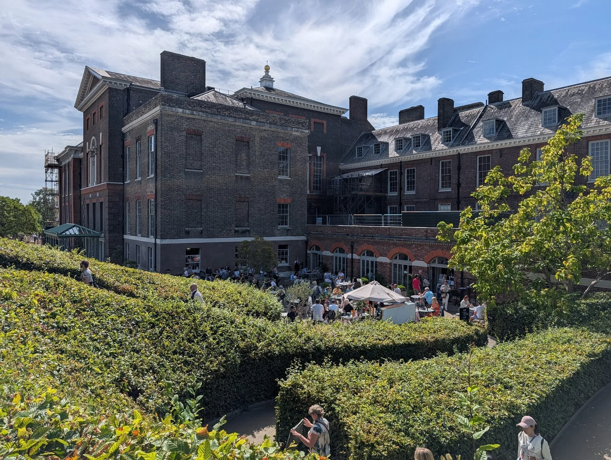 Kensington Palace seen across clipped hedges, with visitors at tables on the lawn beyond